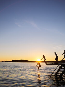Children diving from jetty into sea at sunset