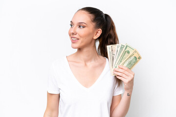 Young caucasian woman taking a lot of money isolated on white background looking to the side and smiling