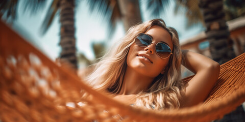 jeune femme blonde avec lunettes de soleil étendue dans un hamac sur la plage avec palmiers - obrazy, fototapety, plakaty
