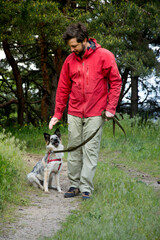 A guy in a red jacket walks his dog in the woods
