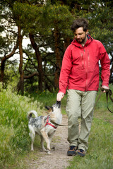 A guy in a red jacket walks his dog in the woods