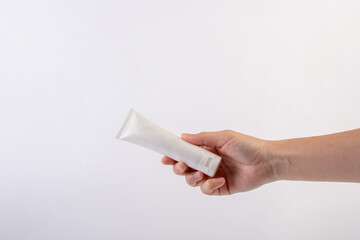 Hand and plastic white tube for cream or lotion. Skin care or sunscreen cosmetic on white background.