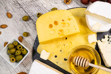 Maasdam cheese with dried apricots, nuts and honey on a graphite board. Top view.