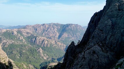 Fototapeta na wymiar Breathtaking Aerial Vista: A Journey Within the 'Trou de la Bombe', Aiguilles de Bavella, Corsica - Majestic Sunlit Peaks and Rugged Terrains Stretching into Infinity