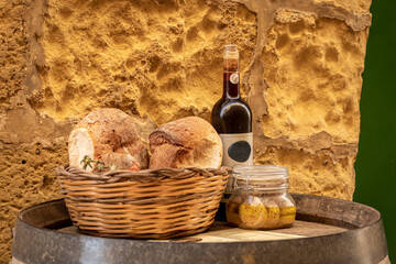 Bottle of wine, artisan bread in wicker basket and marinated cheese in a jar on a wooden barrel....