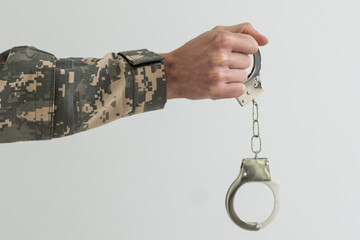 A military man in handcuffs holds an army badge in his hand on a dark background, selective focus....