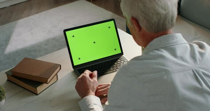 Mockup with grandpa at laptop with green chromakey. Green chromakey on laptop display. Grandpa talking via video chat, video call with his family. Template with grandfather and a chromakey on a laptop