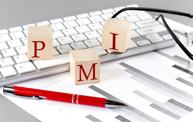 PMI written on a wooden cube on the keyboard with chart on grey background