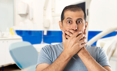 Shocked man with toothache or tooth pain covering his mouth with hands at dentist office