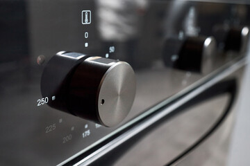Oven knob selective focus stainless steel turned to 250 Celsius degrees over black glass front panel of contemporary modern kitchen bakery professional cooker closeup shot with copyspace.
