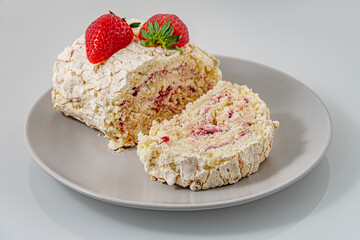 delicious meringue roll with strawberry cream decorated with  fragrant ripe strawberries on a white glass surface