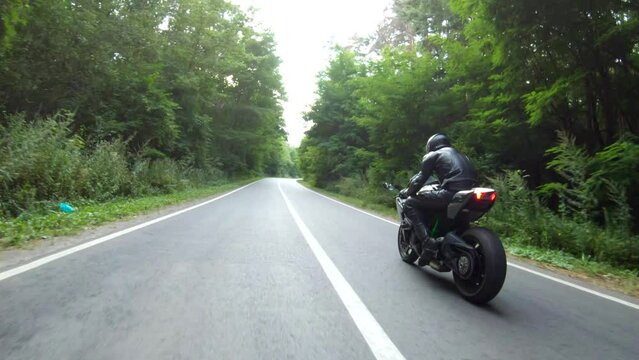 Motorcyclist races motorcycle on woodland country road. Man in helmet rides on sport motorbike at rural road near forest. Guy driving bike during trip. Concept of freedom and adventure. Aerial shot