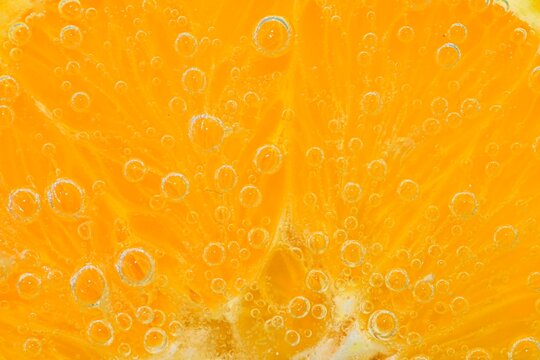 Slice of orange fruit in sparkling water. Orange fruit slice covered by bubbles in carbonated water. Orange fruit slice in water with bubbles. Close-up, macro horizontal image.
