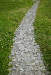 Stone path in perspective on green grass in summer garden. cobble stoned pathway in fresh spring grass meadow. texture background.