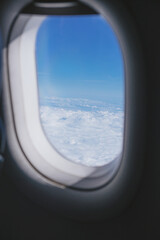 An airplane window with blue sky and cloud outside 