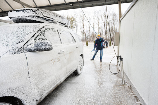 Man washing american SUV car with roof rack at a self service wash in cold weather.