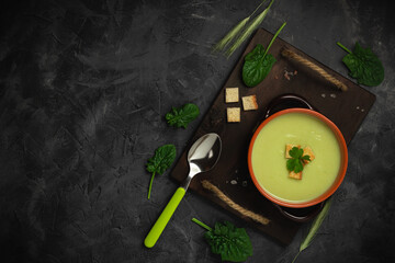 Healthy asparagus soup in a bowl over dark wooden cutting board, concrete background.Top view with copy space.