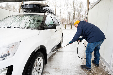 Man washing high pressure water american SUV car with roof rack at self service wash in cold weather.