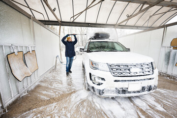 Man washing high pressure water american SUV car with roof rack at self service wash in cold weather.