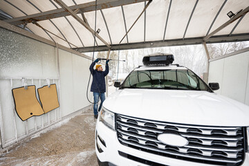 Man washing high pressure water american SUV car with roof rack at self service wash in cold weather.