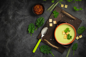Healthy asparagus soup in a bowl over dark wooden cutting board, concrete background.Top view with copy space.
