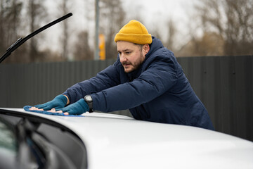 Man wipes american SUV car hood with a microfiber cloth after washing in cold weather.