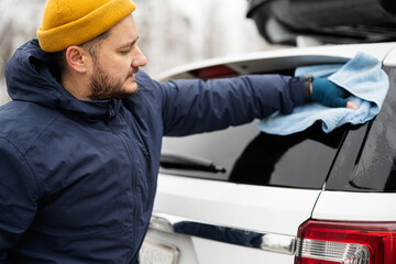 Man wipes american SUV car with a microfiber cloth after washing in cold weather.