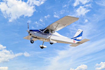 Single engine ultralight plane flying in the blue sky with white clouds	
