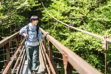 Naklejka na ściany i meble トレッキングをしている若い日本人女性/ 橋を渡る 