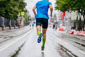 rear view male runner running city marathon on wet road, compression socks on feet, summer sports...
