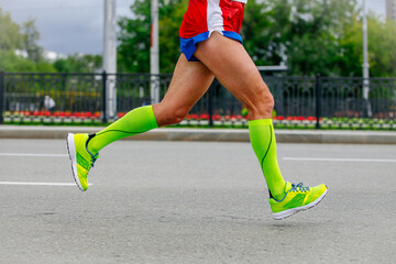 close-up legs runner athlete running marathon in city in green compression socks on feet, sports...