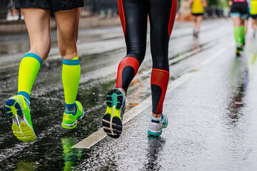 legs female runners running together marathon on wet asphalt, green compression socks and black leggings