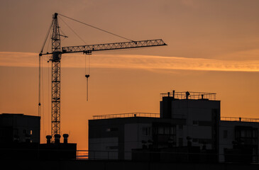 Cranes and buildings under construction against the orange and red sunset sky