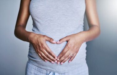 Pregnancy, woman and heart hands on her stomach for love, care and maternity in her house. Bonding, maternal and closeup of a pregnant female person holding her belly for motherhood at her home.