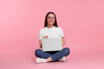 Naklejka premium Smiling young woman with laptop on pink background