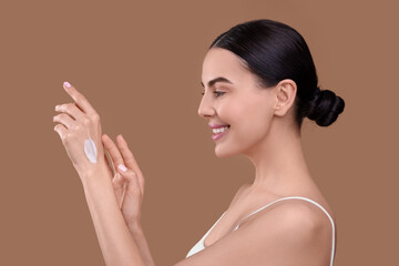 Beautiful woman with smear of body cream on her hand against light brown background