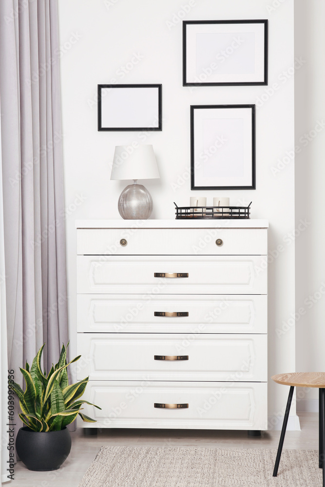 Sticker Empty frames hanging on white wall, chest of drawers and potted plant indoors