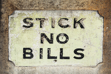 Weathered and worn Stick No Bills signage on the side of a concrete wall