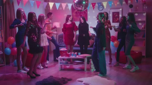 Friends are dancing vigorously at a party. The girl in black stands out among everyone with her informality, modesty and bashfulness. Party at home, in a decorated room with a disco ball.