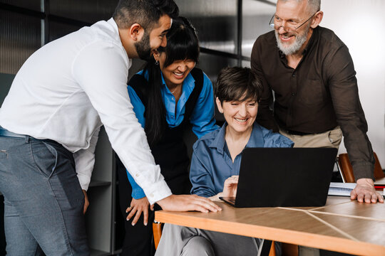 Laughing multicultural colleagues discussing project on laptop at office meeting