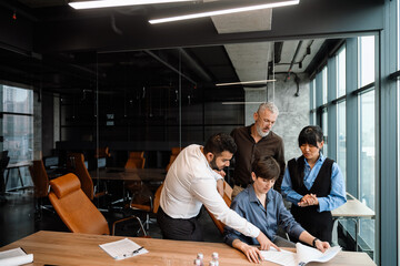 Concentrated multiethnic colleagues checking documents behind boss back and talking in office