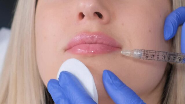 A young woman receives a botox injection in her lips. A woman in a beauty salon. Close up.