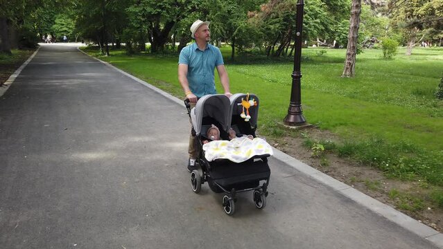 Father with kids in double stroller in a park. Man pushing twins stroller, pram.