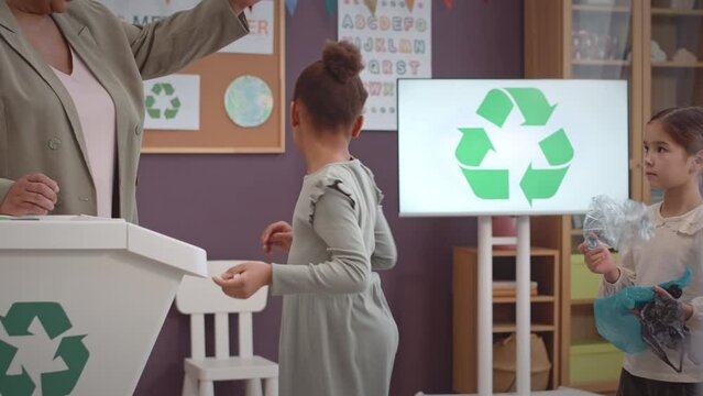 Diverse first grade pipuls and their teacher taking part in eco project together at school, sorting rubbish in containers for further recycling