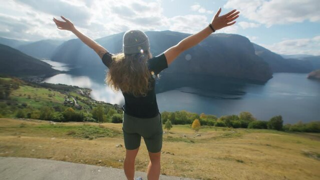 Exciting and fun shot of young woman run towards epic view on fjord in Norway. Jumps on top of rocks, raises arms into air, happy and drunk on life, youth and happiness. Freedom and travel blogger 