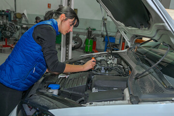 Young female mechanic, working on the repair of a car engine.