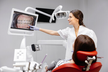 Caucasian dentist woman explaining xray on screen to female patient at clinic
