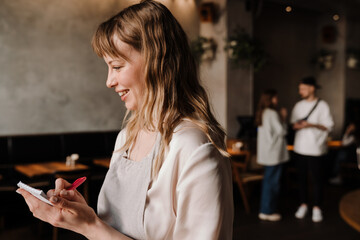 Cute young blonde waitress writes down order in cafe