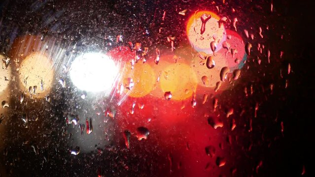 Headlights and rear red lights of cars through the wet glass of a car. Beautiful multi-colored stains of light refraction through wet glass.