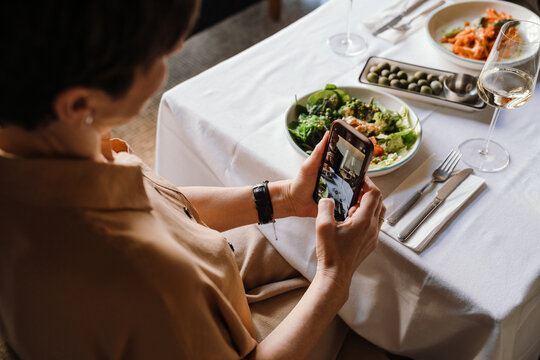Top view of mature woman takes pictures of food on cell phone on date with husband in cafe